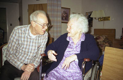 An old person talking to an elderly person in a wheelchair

Description automatically generated