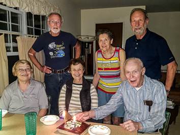 A group of people around a table with a cake and candles

Description automatically generated